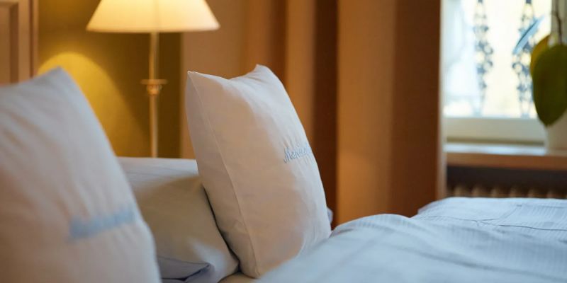 Gemachtes Bett mit weissen Kissen und Lampe im warm beleuchteten Schlafzimmer